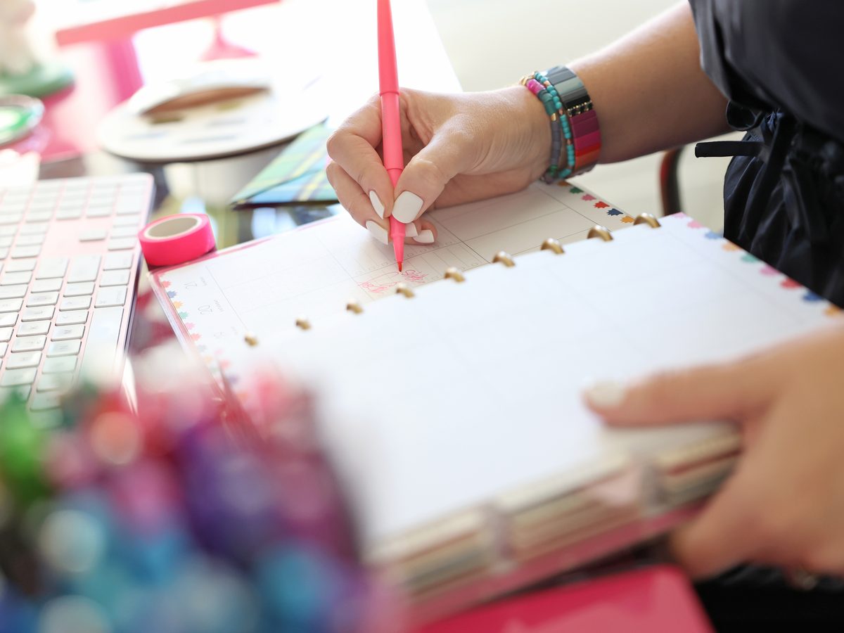 Sarah writing in a planner with a pink pen, a jar of coloured pens in the foreground