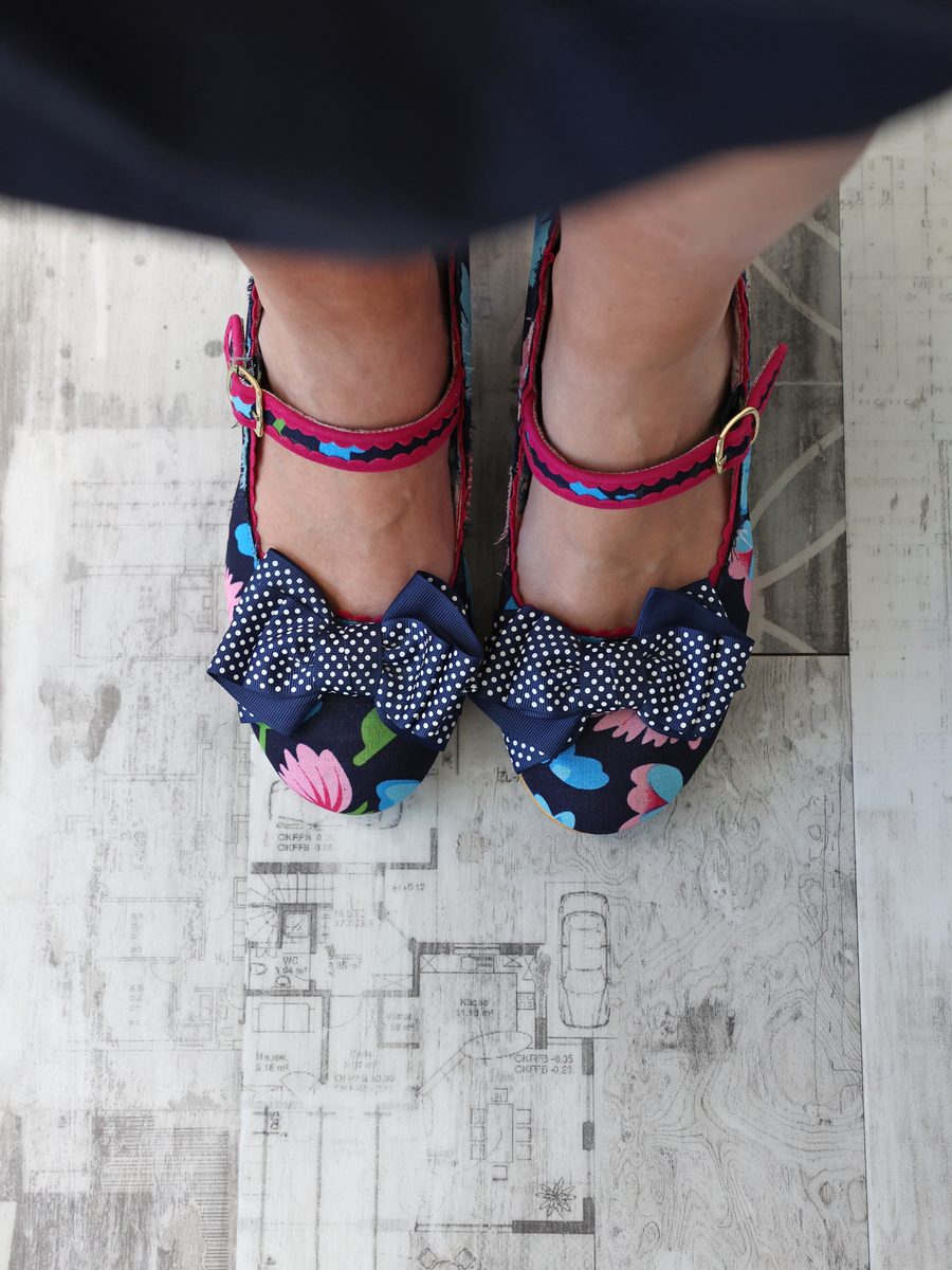 Overhead view of Sarah&rsquo;s navy floral heels with polka-dot bows, standing on a printed floor plan