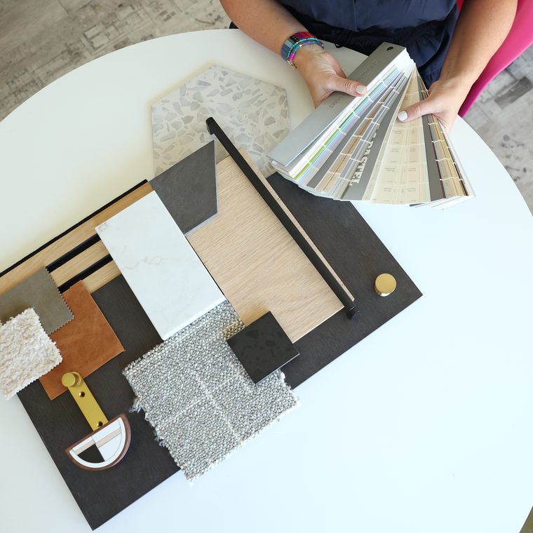 Overhead view of a finished material board — flooring, marble, leather, bouclé and terrazzo — with a paint fan deck in hand