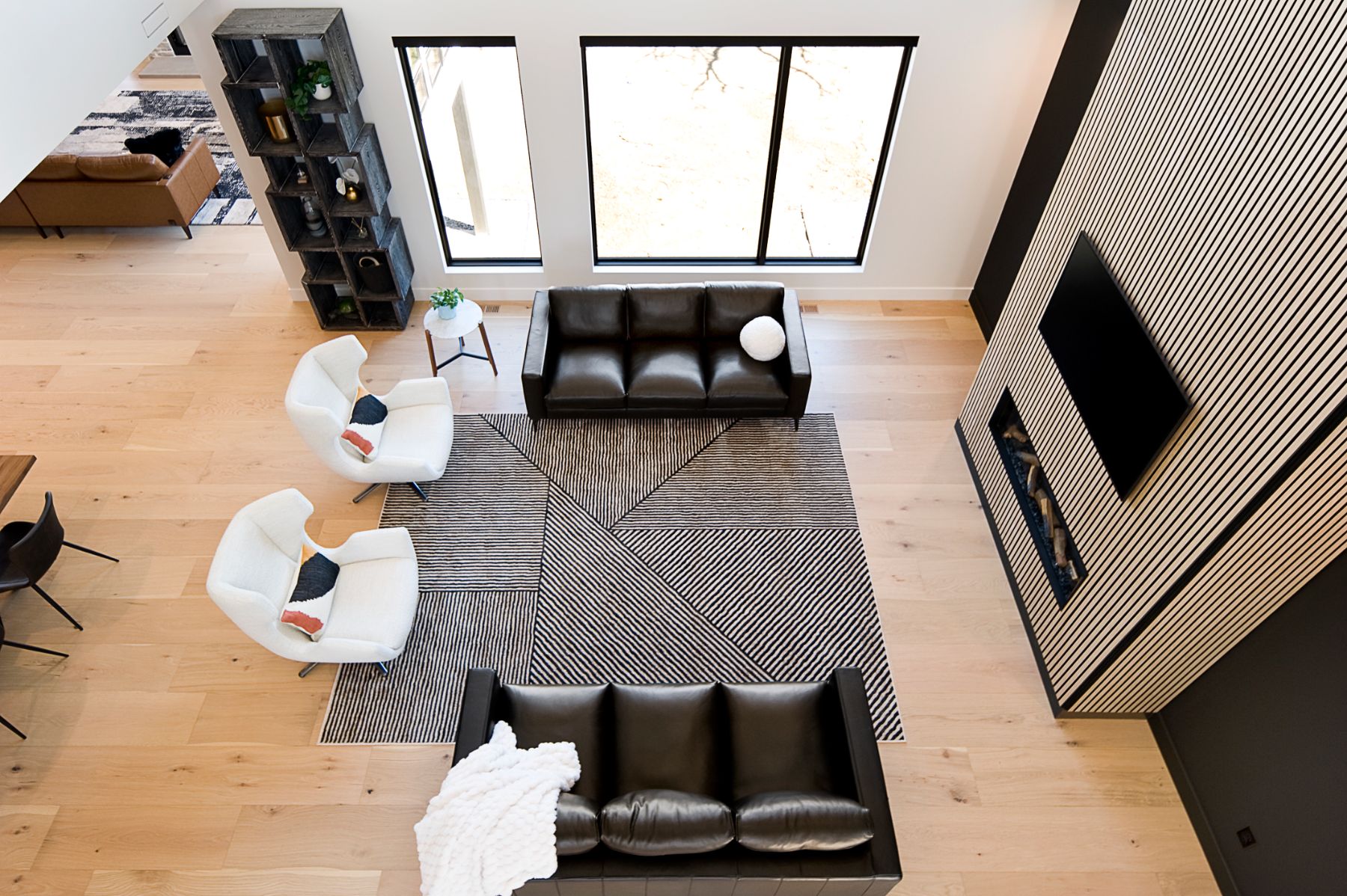 Great room from the loft above, black sectional and white chairs on a striped rug