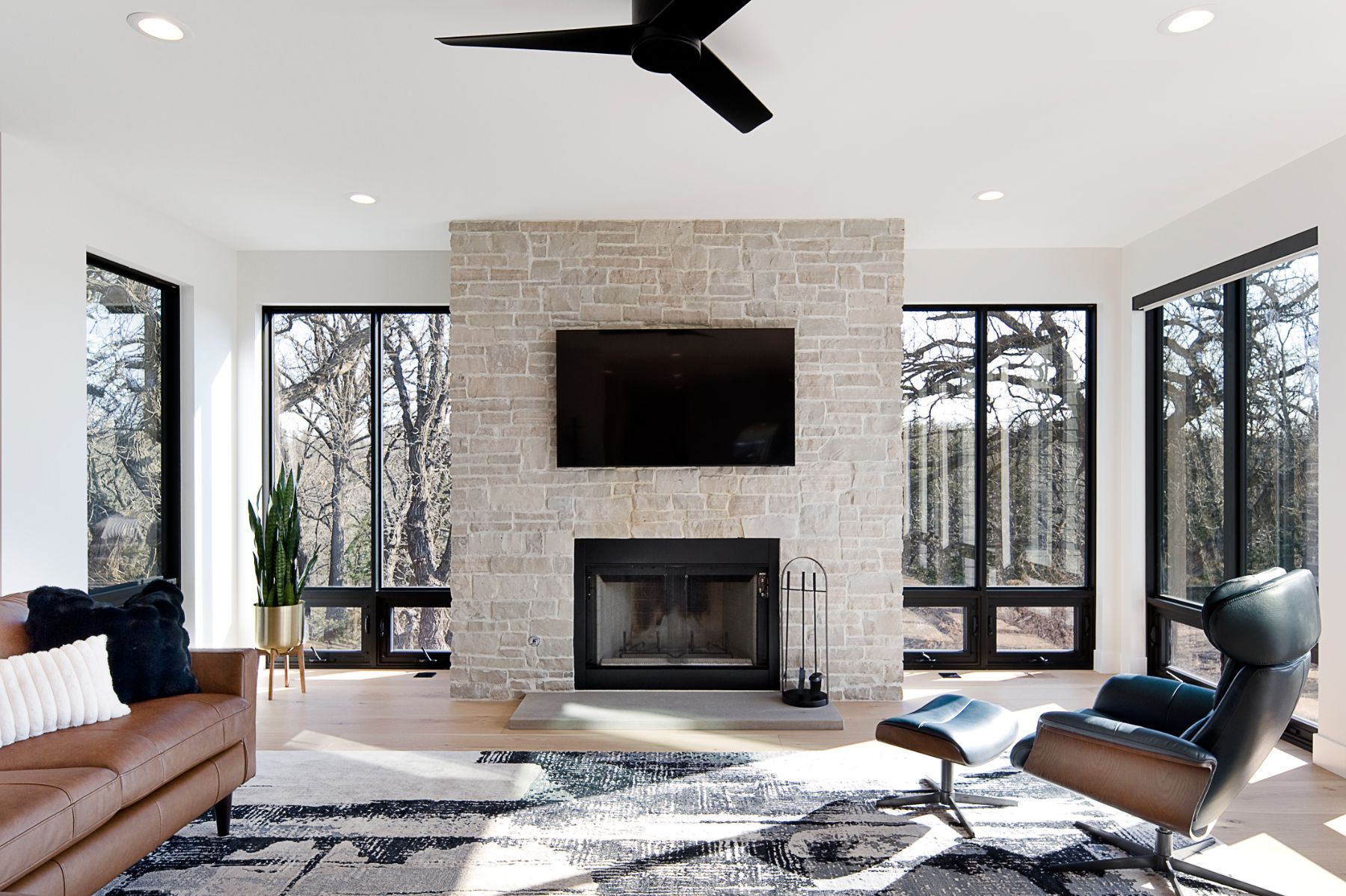 Great room with a stone fireplace, black window frames and leather seating