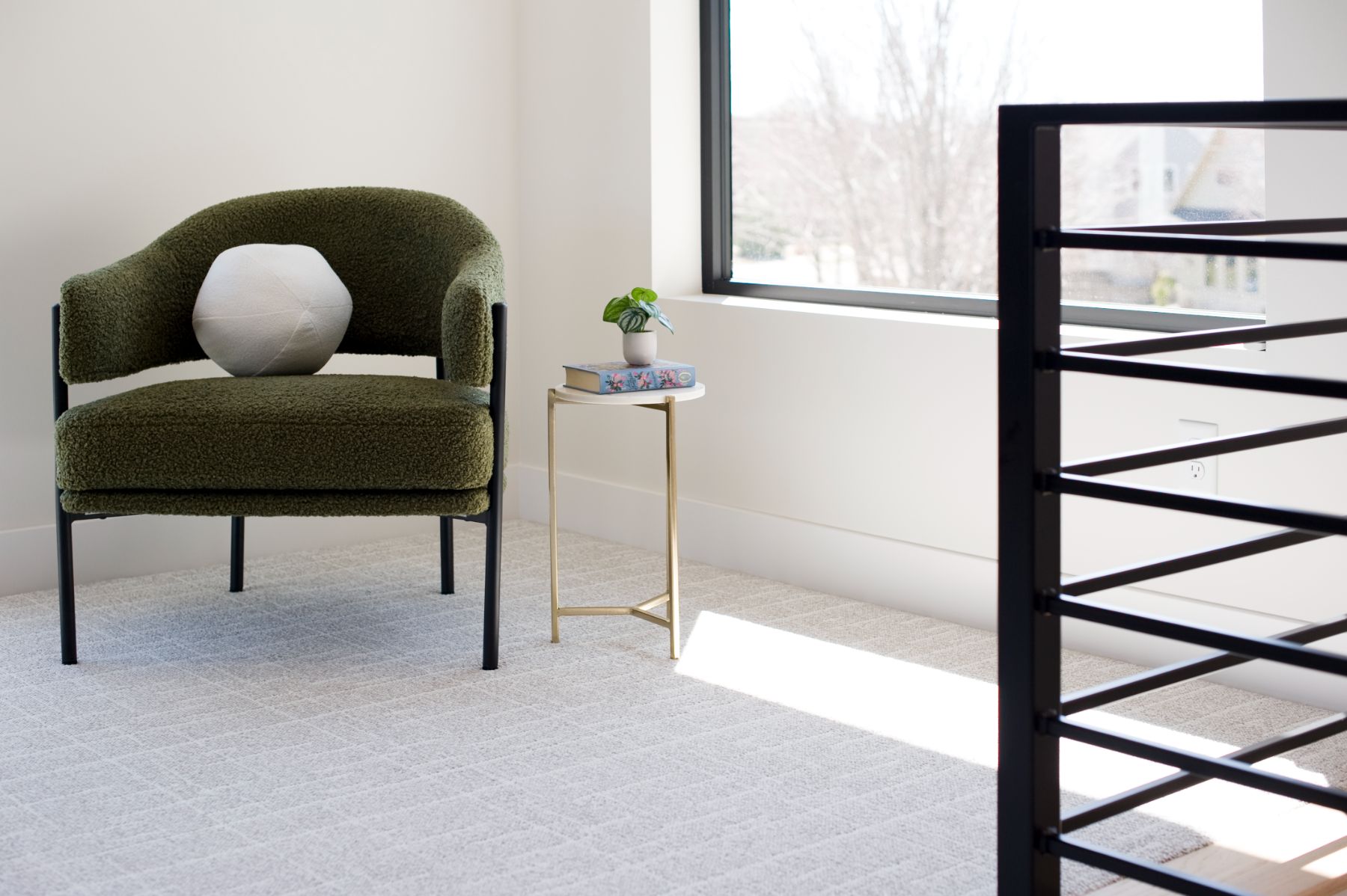 Olive bouclé chair at the top of the stairs beside a black steel rail