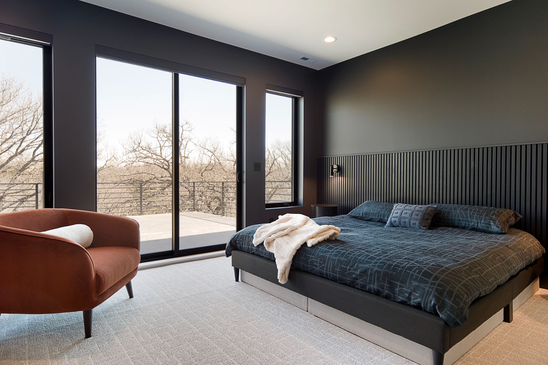 Primary bedroom with a black slat headboard wall and a rust chair