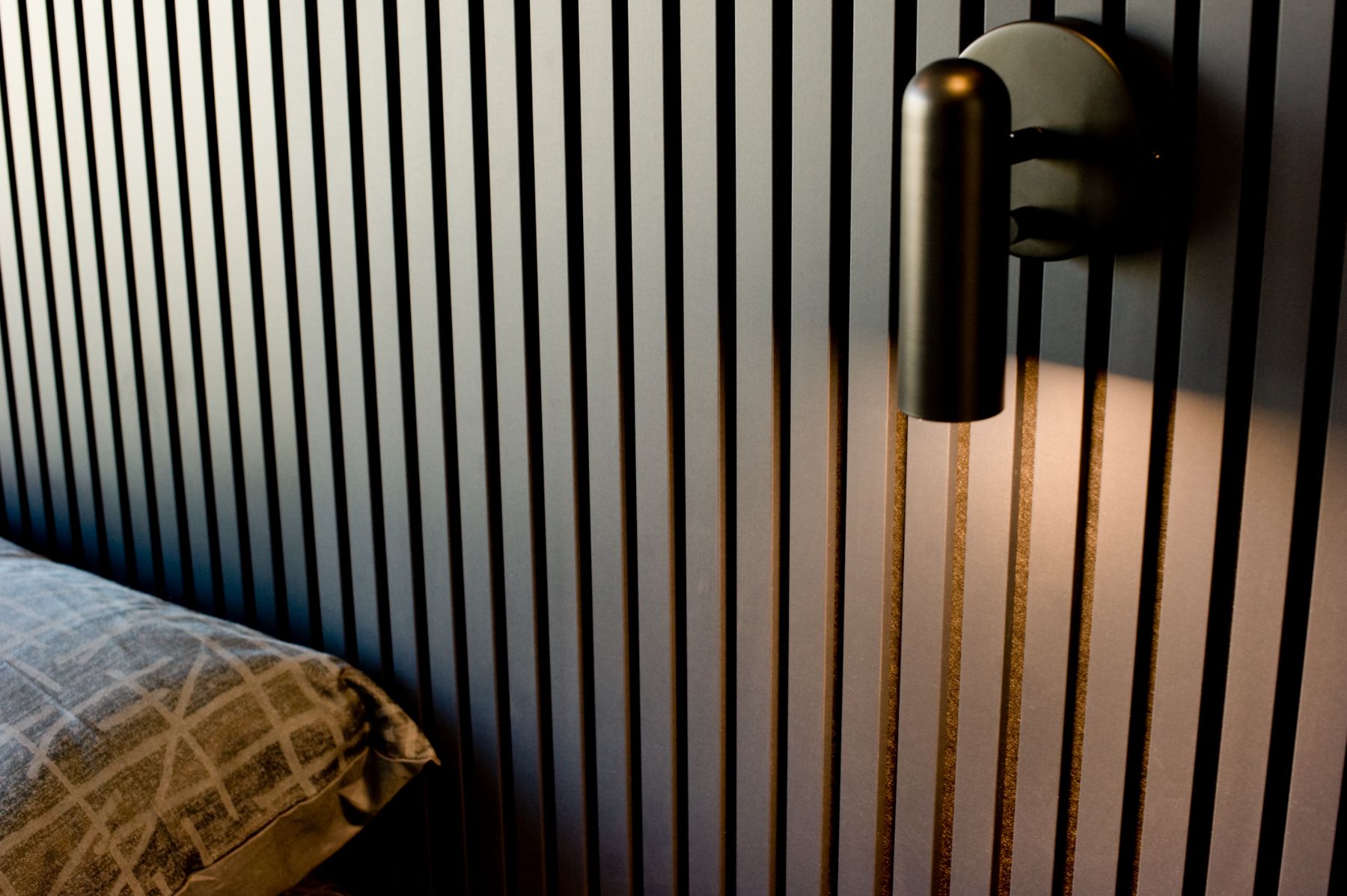 Black slat wall detail with a wall sconce