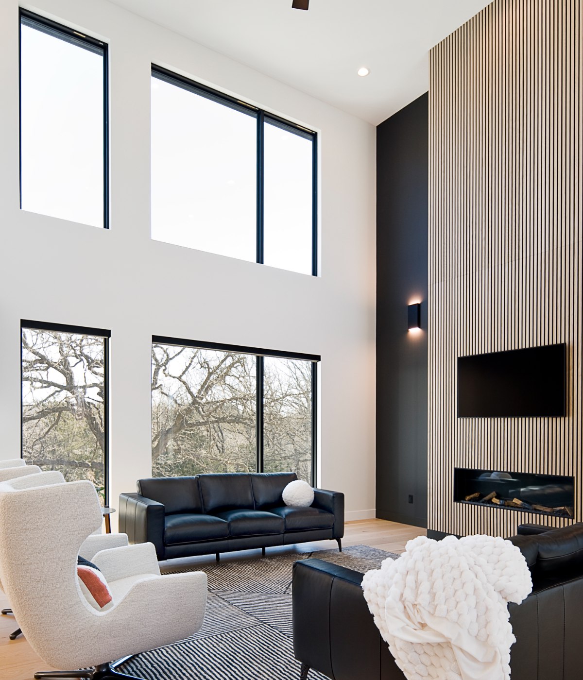 A two-story great room with a black slat feature wall, stone fireplace, and white oak floors